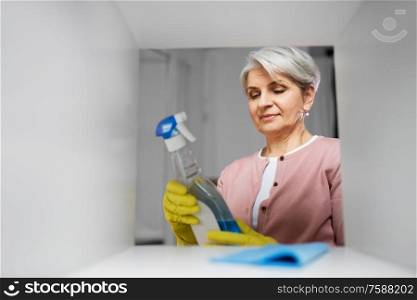 people, housework and housekeeping concept - happy senior woman cleaning rack and reading label on detergent at home. senior woman cleaning rack with detergent at home
