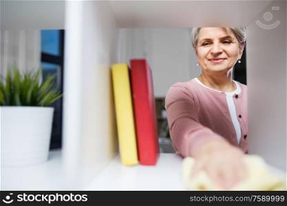 people, housework and housekeeping concept - happy senior woman with dusting cloth cleaning rack at home. happy senior woman with cloth dusting rack at home