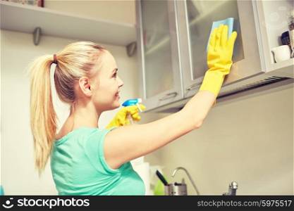people, housework and housekeeping concept - happy woman cleaning cabinet with rag and cleanser at home kitchen