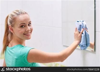 people, housework and housekeeping concept - happy woman cleaning mirror with rag at home