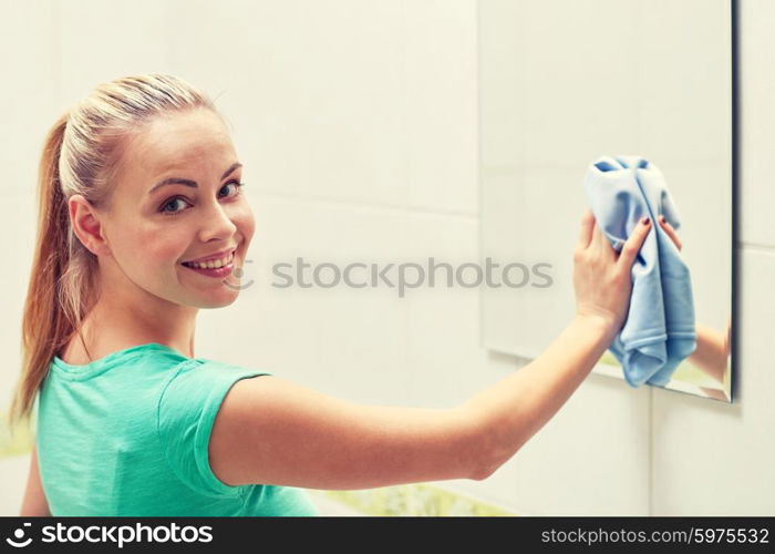 people, housework and housekeeping concept - happy woman cleaning mirror with rag at home