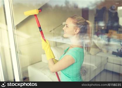 people, housework and housekeeping concept - happy woman in gloves cleaning window with sponge mop at home