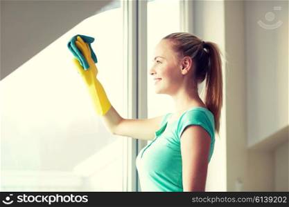 people, housework and housekeeping concept - happy woman in gloves cleaning window with rag at home