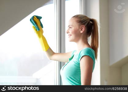 people, housework and housekeeping concept - happy woman in gloves cleaning window with rag at home