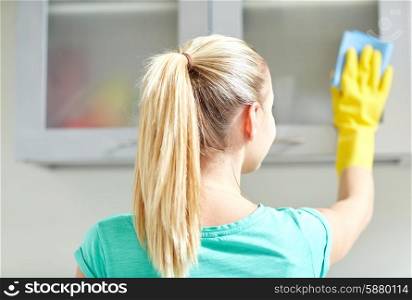 people, housework and housekeeping concept - happy woman in protective gloves cleaning cabinet with rag at home kitchen