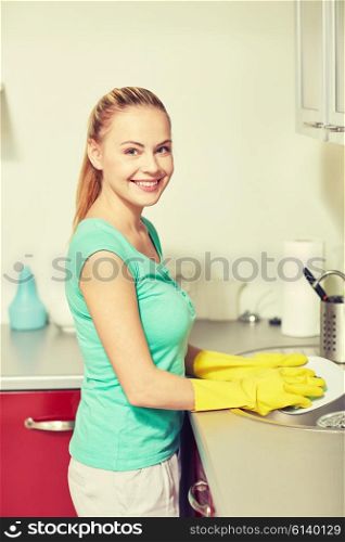 people, housework and housekeeping concept - happy woman in protective gloves washing dishes at home kitchen