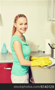 people, housework and housekeeping concept - happy woman in protective gloves washing dishes at home kitchen