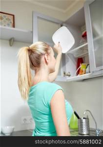 people, housework and housekeeping concept - happy woman putting plate to kitchen cabinet