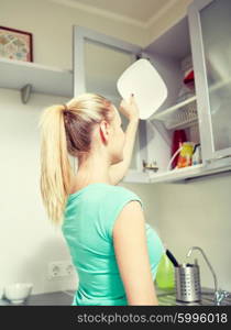 people, housework and housekeeping concept - happy woman putting plate to kitchen cabinet
