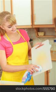 People, housework and housekeeping concept. Woman doing the tidying up in kitchen cleaning plastic cutting board with rag sponge