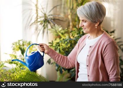 people, housework and plants care concept - senior woman watering houseplants at home. senior woman watering houseplants at home