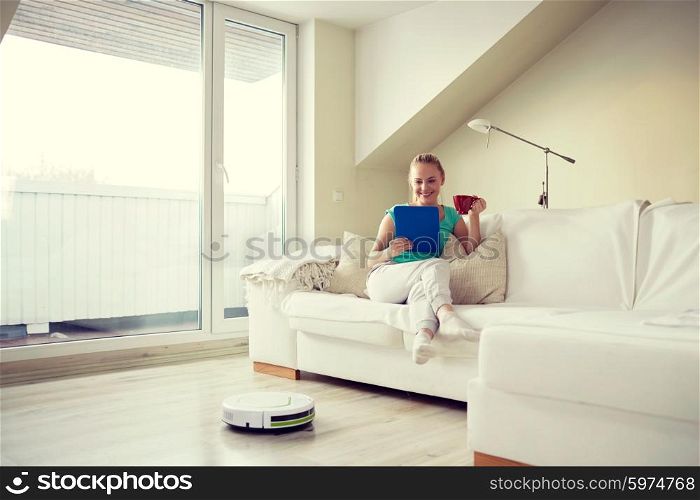 people, housework and technology concept - happy woman with tablet pc computer and robot vacuum cleaner drinking tea at home