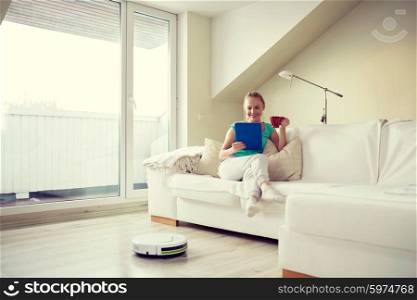 people, housework and technology concept - happy woman with tablet pc computer and robot vacuum cleaner drinking tea at home