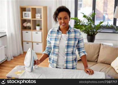 people, housework, laundry and housekeeping concept - happy african american woman ironing bed linen on board at home. african american woman ironing bed linen at home