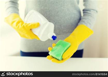 people, housework, washing-up and housekeeping concept - close up of woman applying liquid soap from cleanser bottle to sponge at home