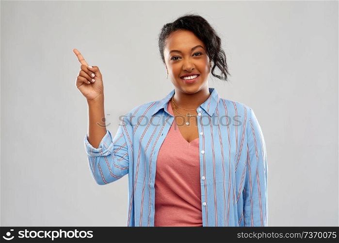 people, idea and attention concept - happy african american young woman pointing finger up over grey background. happy african american woman pointing finger up