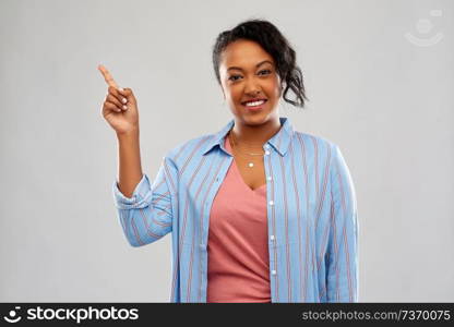 people, idea and attention concept - happy african american young woman pointing finger up over grey background. happy african american woman pointing finger up