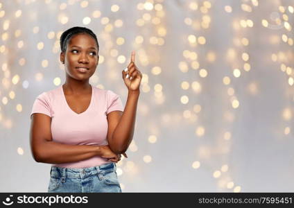 people, idea and holidays concept - happy african american young woman pointing finger up over festive lights background. happy african american woman pointing finger up