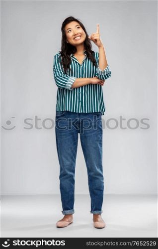 people, idea and inspiration concept - happy smiling asian young woman pointing finger up over grey background. happy smiling asian woman pointing finger up