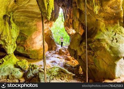 People in big dark cave- silhouette of woman in cave and sun light from jungle forest