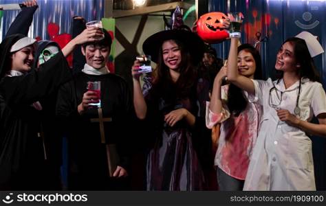 People in halloween costume dancing, having fun and drinking together in party at night