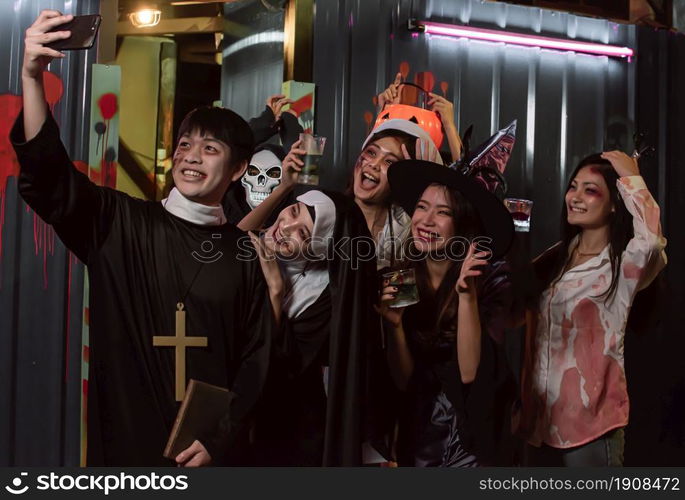 People in halloween costume dancing, having fun, taking selfie and drinking together in party at night