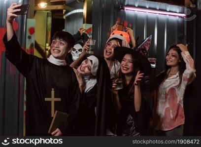 People in halloween costume dancing, having fun, taking selfie and drinking together in party at night