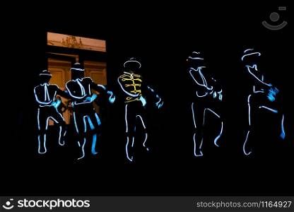 People in luminous costumes dance in the dark for a holiday. People in glowing costumes dancing in the dark