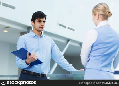 People indoors having talk. Businessman and woman in modern interior holding document case and talking to her colleague