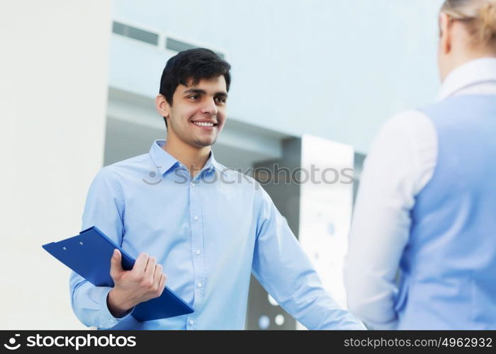 People indoors having talk. Businessman and woman in modern interior holding document case and talking to her colleague