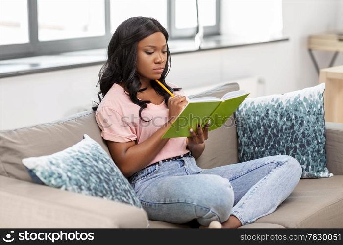 people, inspiration and leisure concept - african american woman with diary sitting in chair at home. african american woman with diary at home