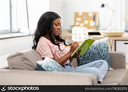 people, inspiration and leisure concept - african american woman with diary sitting in chair at home. african american woman with diary at home