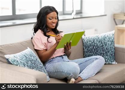 people, inspiration and leisure concept - happy smiling african american woman with diary sitting in chair at home. happy african american woman with diary at home