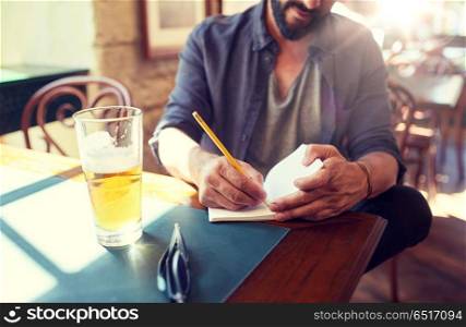 people, inspiration, freelance and leisure concept - close up of man with beer writing to notebook at bar or pub. close up of man with beer and notebook at pub. close up of man with beer and notebook at pub