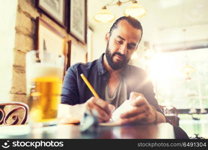 people, inspiration, freelance and leisure concept - man with beer writing to notebook at bar or pub. man with beer writing to notebook at bar or pub. man with beer writing to notebook at bar or pub