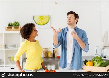 people, international and healthy eating concept - happy couple cooking food and juggling garlic at home kitchen. couple cooking food and juggling garlic at home