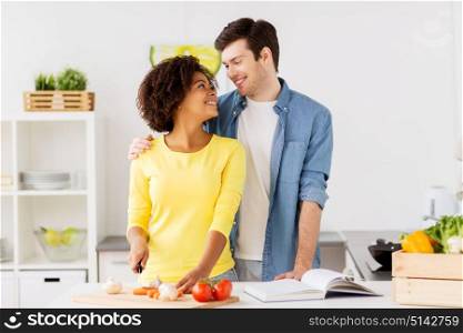 people, international and healthy eating concept - happy couple cooking food and chopping vegetables at home kitchen. happy couple cooking food at home kitchen