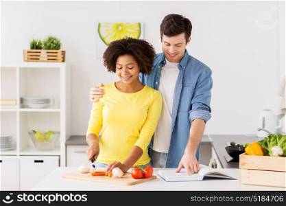 people, international and healthy eating concept - happy couple cooking food and chopping vegetables at home kitchen. happy couple cooking food at home kitchen