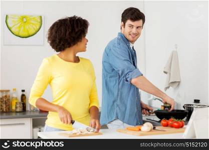 people, international and healthy eating concept - happy couple cooking food and talking at home kitchen. happy couple cooking food at home kitchen