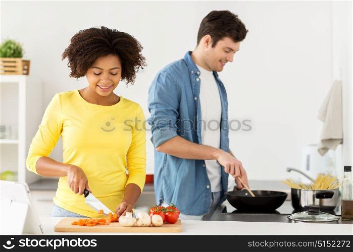 people, international and healthy eating concept - happy couple cooking food at home kitchen. happy couple cooking food at home kitchen