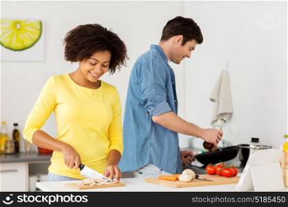 people, international and healthy eating concept - happy couple cooking food at home kitchen. happy couple cooking food at home kitchen