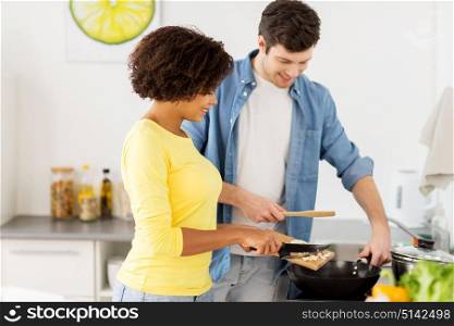 people, international and healthy eating concept - happy couple with frying pan cooking food at home kitchen. happy couple cooking food at home kitchen