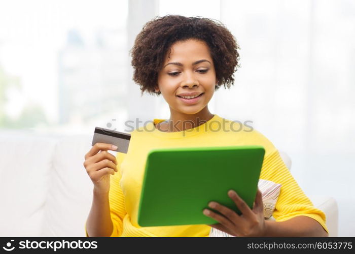 people, internet bank, online shopping, technology and e-money concept - happy african american young woman sitting on sofa with tablet pc computer and credit card at home