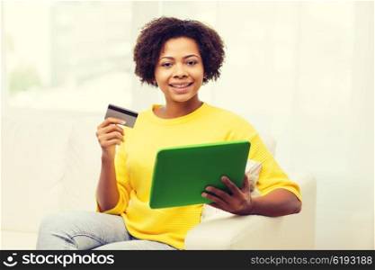 people, internet bank, online shopping, technology and e-money concept - happy african american young woman sitting on sofa with tablet pc computer and credit card at home