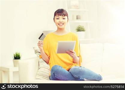 people, internet bank, online shopping, technology and e-money concept - happy asian young woman sitting on sofa with tablet pc computer and credit card at home. happy asian woman with tablet pc and credit card