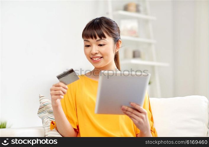 people, internet bank, online shopping, technology and e-money concept - happy asian young woman sitting on sofa with tablet pc computer and credit card at home