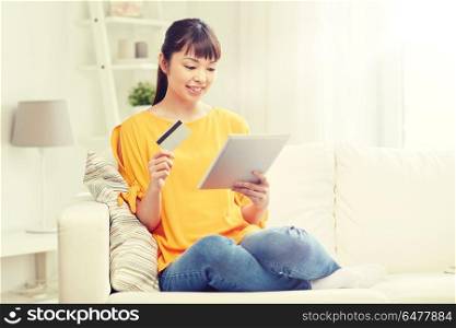 people, internet bank, online shopping, technology and e-money concept - happy asian young woman sitting on sofa with tablet pc computer and credit card at home. happy asian woman with tablet pc and credit card. happy asian woman with tablet pc and credit card
