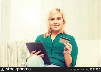 people, internet bank, online shopping, technology and e-money concept - happy young woman sitting on sofa with tablet pc computer and credit card at home. happy woman with tablet pc and credit card