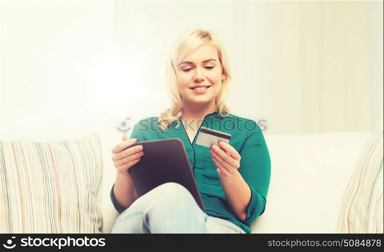 people, internet bank, online shopping, technology and e-money concept - happy young woman sitting on sofa with tablet pc computer and credit card at home. happy woman with tablet pc and credit card. happy woman with tablet pc and credit card