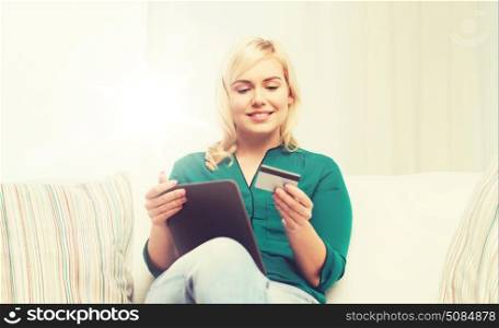 people, internet bank, online shopping, technology and e-money concept - happy young woman sitting on sofa with tablet pc computer and credit card at home. happy woman with tablet pc and credit card. happy woman with tablet pc and credit card